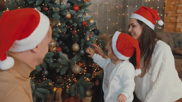 Happy Family Sitting While Their Little Girl Plays with the Toys on the Tree.