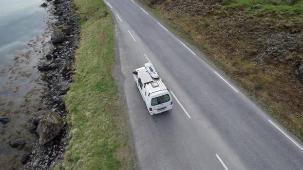 Aerial view of a camping van starting out on a journey on a road along a very calm fjord