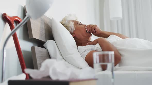 Sick african american senior woman holding tissue coughing while lying on the bed at home