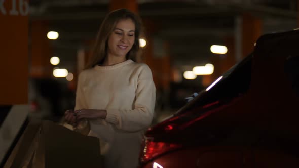 The Girl with a Smile on Her Face Opens the Trunk of the Car and Puts Paper Shopping Bags  Slow Mo