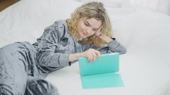 Young Relaxed Caucasian Woman Surfing Social Media on Tablet in the Morning in Bedroom