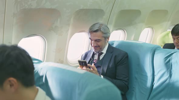 Caucasian senior elder business man in formal suit wear earphones, enjoy listen to music on airplane