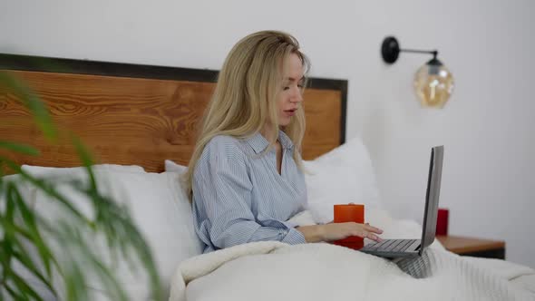 Side View of Confident Busy Caucasian Woman Typing on Laptop Keyboard Sitting in Bed at Night