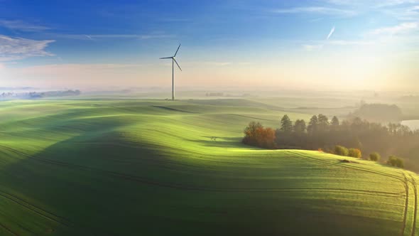 Foggy wind turbine on green field at sunrise