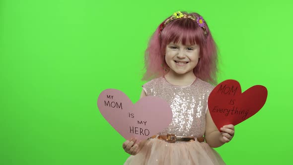 Child Girl Princess Holds Two Paper Hearts with Text About Mother. Mother's Day