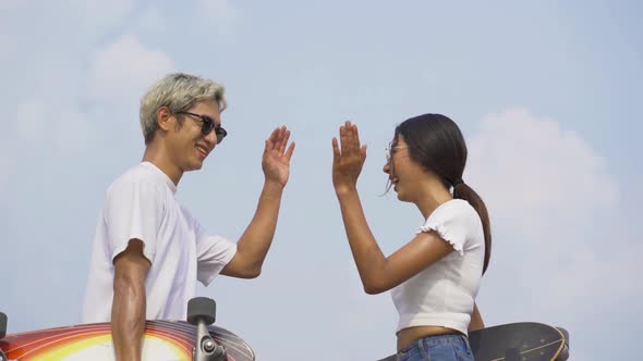 Portrait of young Asian couple giving high five to each others while holding skateboard