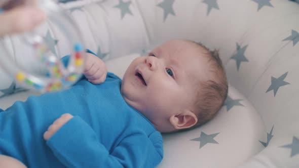 Happy Little Baby Bothers Arms Looking at Rattle in Cocoon