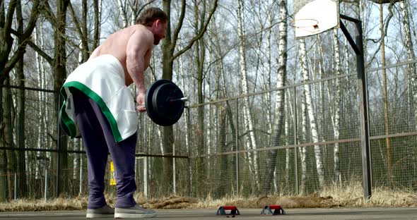 Bodybuilder Is Training Outdoors, Lifting Weights in Sporty Area in Park in Spring Day