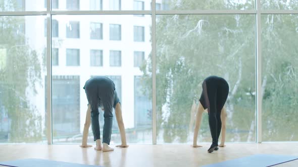 Young Woman and Mid-adult Man Standing on Hands Against Floor-to-ceiling Window. Wide Shot of