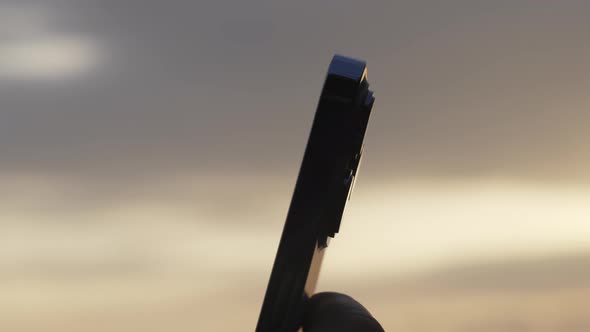 A Closeup of a New Modern Phone in the Hands of a Man Against the Background of a Wonderful Sunset