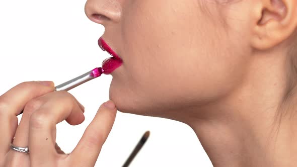 Macro Shot in Profile of Beautiful Sexy Woman Putting on Pink Lipstick with Lip Brush Over White