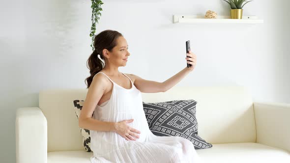 Pregnant Woman Makes Selfie with Smartphone Sitting on Sofa