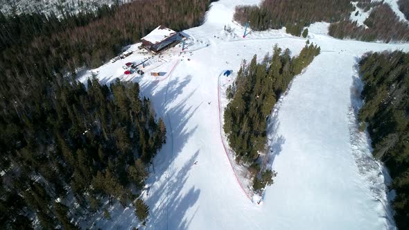 Aerial Top Down View on a Ski Slope Surrounded with Trees People Snowboarding and Skiing Down the