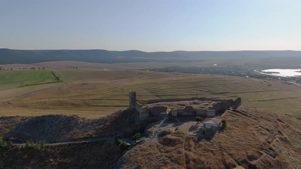 Long drone tracking shot of Enisala, medieval fortress on top of a hill surrounded by lakes and plai