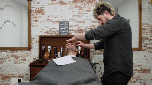 Barber Shaving Bearded Male with a Sharp Razor