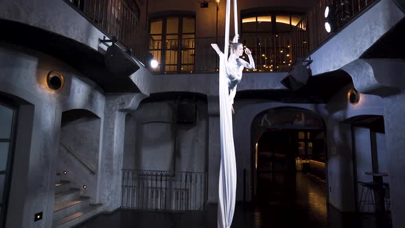 Female aerialist doing a front split pose on silks with her knees bent.