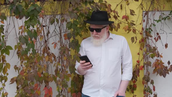 Old Man with Albinism Surfing the Internet While Sitting Next To His House