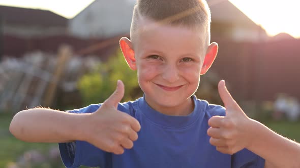 Excited boy showing thumbs up looking at camera and smiling outdoors. Portrait of happy cheerful kid