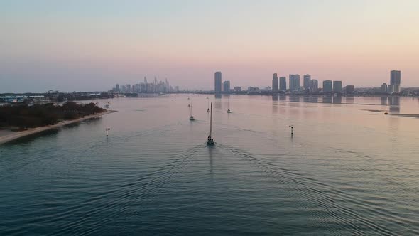 A high view of a group of yachts at sunset entering a harbour with a smoke haze city skyline in the