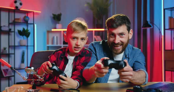 Man and Teen Boy Having Fun Together at Home in the Evening while Playing videogames