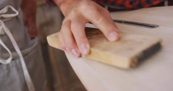 Two Caucasian male surfboard makers working in their studio and making a wooden surfboard together