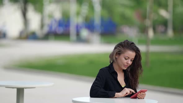 Woman with Smartphone in Street Cafe in Park Area at Summer Day Sending Messages in Social Nets