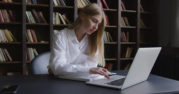 Business Woman in a White Shirt Works at a Laptop and Takes Notes