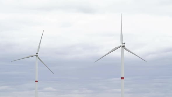 Motion the Blades of a Large Wind Turbine in a Field Against a Background of Cloudy Grey Sky on the