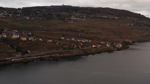 Wide aerial of train driving over railway near small village in the hills