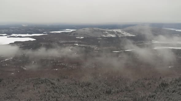 Low hanging clouds over an endless winter forest with lakes and hills AERIAL