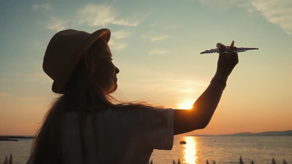 Silhouette Girl Plays with a Toy Airplane on Tropical Beach at Sunset. Hand with Small Plane Close