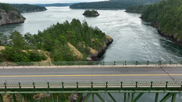 Drone shot pulling away from cars driving on Deception Pass steel bridge.