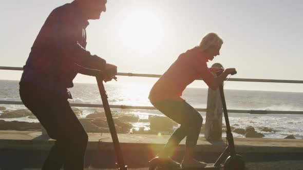 Senior couple using electronic scooters alongside beach