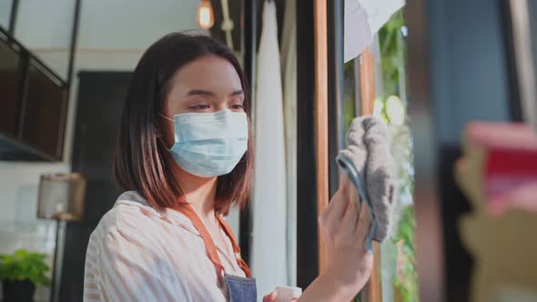 Caucasian cafe waitress wear mask, clean mirror with disinfectant and wipe before welcome customer.