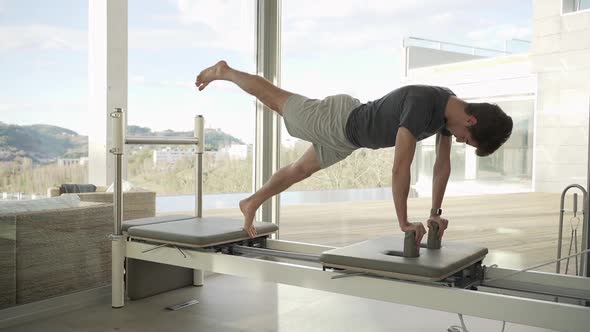 Man doing yoga in One Legged Plank pose on pilates reformer