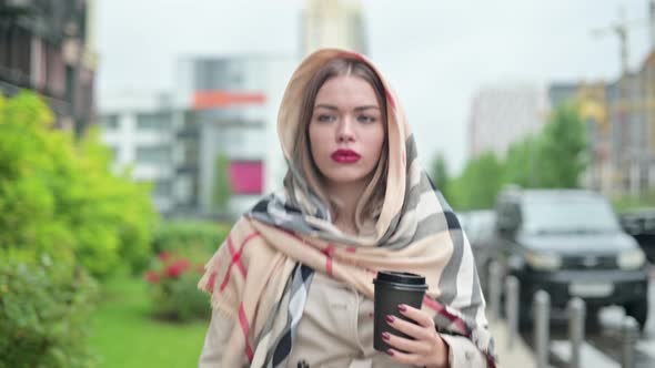Close-up of a young woman walking down the street with a cup of coffee in hands
