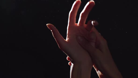 Silhouette Portrait of Two Caucasian Female Arms Closeup Rubbing Hands in Light with Flying Dust