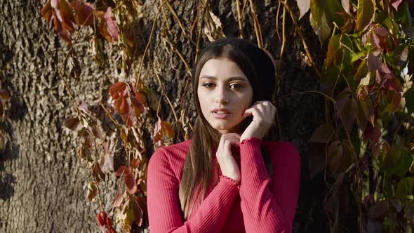 Girl in Stylish Clothes Poses and Caresses Her Face at Autumn Tree Trunk