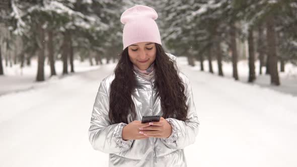 Attractive Girl Walks Through the Winter Forest and Uses a Smartphone