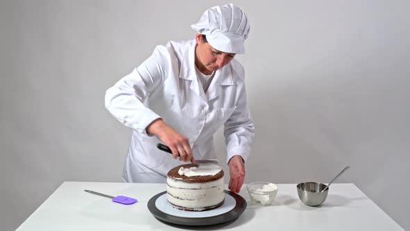 Front Shot of a Baker Using an Icing Spatula To Carefully Touch Up Sides of Cream Covered Cake