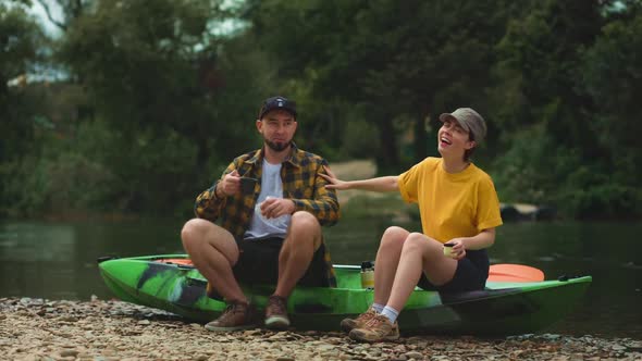 A young couple is sitting on a kayak, and they are eating lunch together