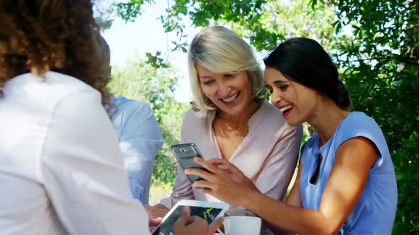 Female friends discussing over mobile phone at outdoor cafe