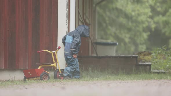 SLOW MOTION - A cute child plays with a downpipe in heavy rainfall