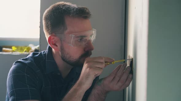 Nervous Man Repairs Plug on Wall with Screwdriver in Room