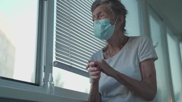 Senior Woman Applying Hand Sanitizer Wearing Protection Mask Against Covid19 Standing By the Window