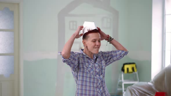 Slim Joyful Redhead Pierced Woman Putting on Paper Hat Gesturing Looking at Camera