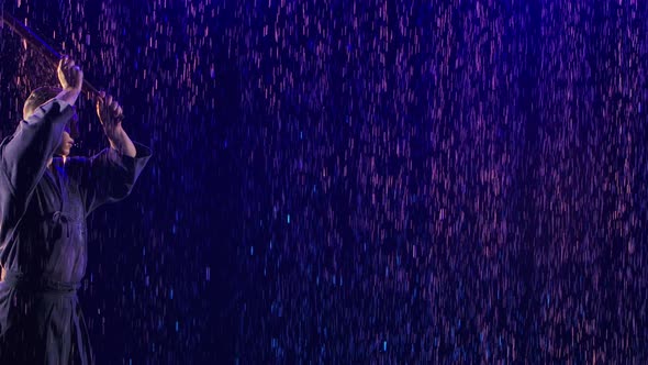 Japanese Kendo Fighter in Traditional Kimono Practicing Martial Skill Among Raindrops on Dark Studio