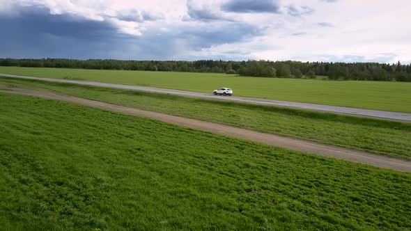 White Modern Automobile Drives Along Gray Asphalt Road