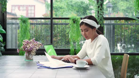 young smiling asian woman working on laptop while enjoying drinking coffee in living room at home