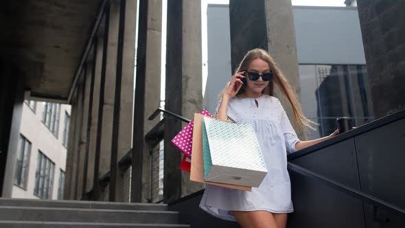 Girl Staying Near Mall with Shopping Bags and Talking on Mobile Phone About Sale on Black Friday